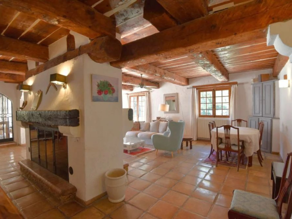 Cozy rustic living and dining area with exposed wooden beams, a large fireplace, and terracotta tiled floor.