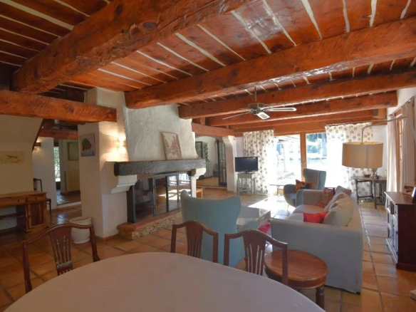 Living room with exposed wood beams, a stone fireplace, and blue couches around a coffee table in a rustic home.