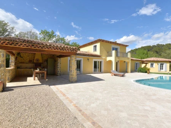 Sunny Mediterranean villa with yellow walls, stone columns, and a curved pool under a blue sky.