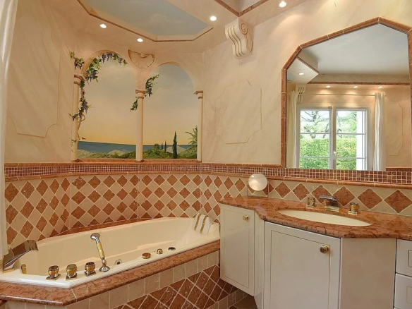 Luxurious bathroom with a corner whirlpool tub, diamond-tiled border, and marble countertop under a large ornate mirror.