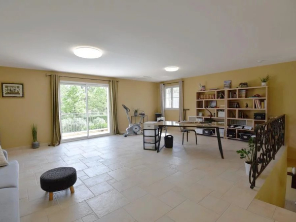 Bright home office and living area with a desk, bookshelf, and exercise bike near a sliding glass door to a balcony.
