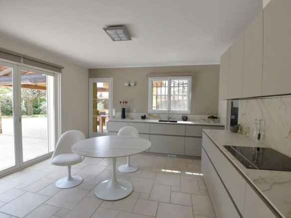 Bright modern kitchen with a white round pedestal table and two matching chairs, marble countertops, and large sliding doors to an outdoor patio.