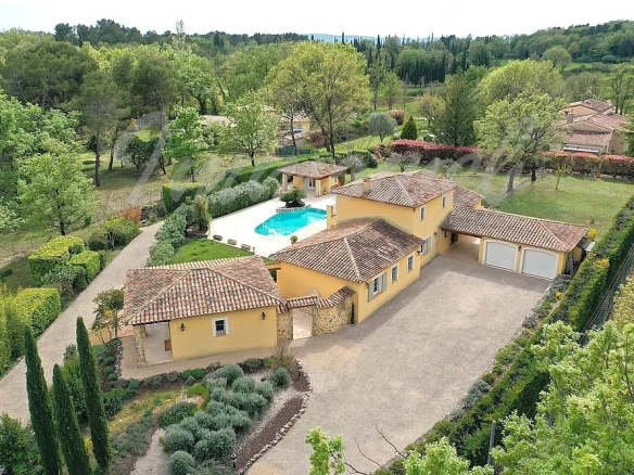 A Mediterranean-style villa with yellow stucco walls, red-tiled roofs, and a blue rectangular pool in a landscaped estate.