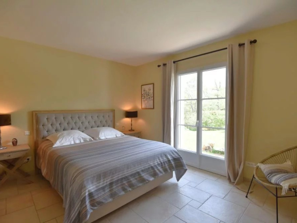 Bright bedroom with a large tufted headboard bed, two nightstands with lamps, and French doors opening to a garden.