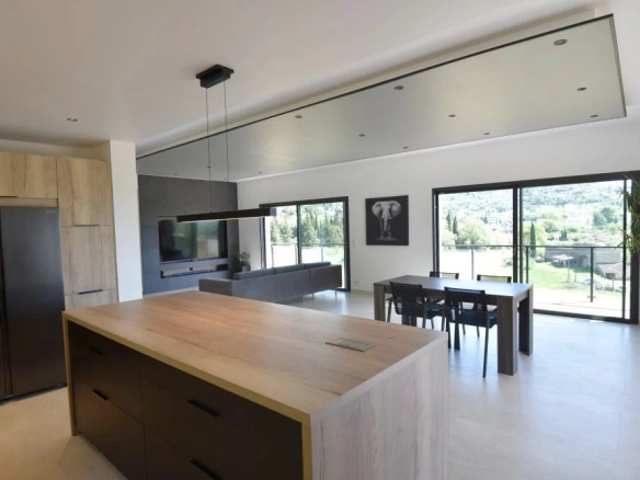 Open-concept kitchen and dining area with a large wooden island, stainless refrigerator, and a dining table beside sliding glass doors showing a green hillside view.