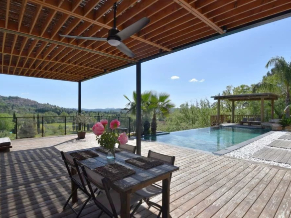 Outdoor deck area with a rectangular pool, mountain view, and a wooden dining table set for four under a covered patio with a ceiling fan.