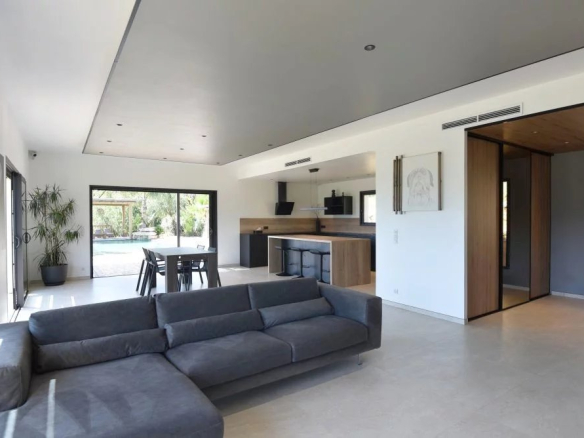 Open-plan living area with a gray sectional sofa, dining table, and kitchen island, opening to a sliding glass door and pool patio.