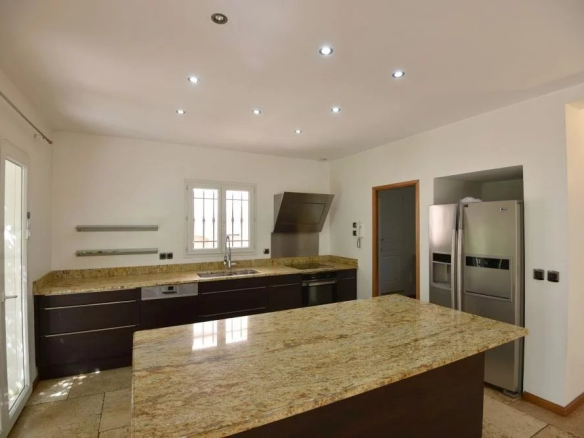 Modern kitchen with a granite island, dark cabinets, and stainless steel appliances including a fridge and double ovens.