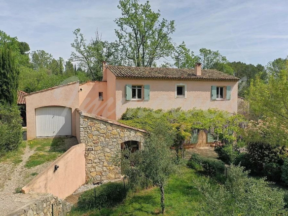 Two-story countryside villa with peach stucco and green shutters, set among trees with a stone terrace and garage