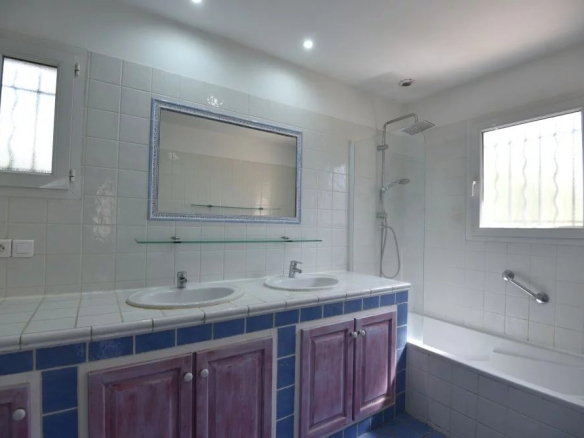 Bright bathroom with a double-sink vanity, blue tile trim, and purple cabinets, plus a bathtub and glass shower area.