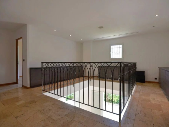 Interior landing with a decorative iron railing overlooking a stairwell to a lower level, tiled floor and white walls, small window ahead.