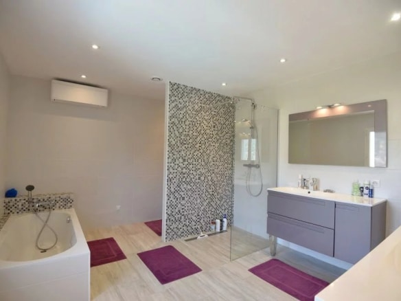 Salle de bain moderne avec douche et baignoire, décorée avec des carreaux et des serviettes violettes.