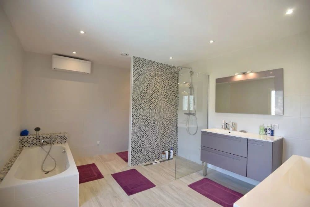 Salle de bain moderne avec douche et baignoire, décorée avec des carreaux et des serviettes violettes.