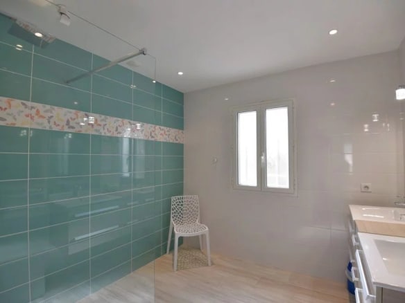 Salle de bain moderne avec carrelage turquoise et meuble lavabo, lumière naturelle par fenêtre.