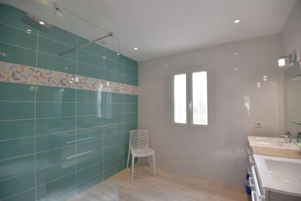 Salle de bain moderne avec carrelage turquoise et meuble lavabo, lumière naturelle par fenêtre.