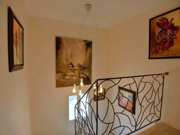 Escalier intérieur d'une villa avec œuvres d'art aux murs et lumière suspendue.