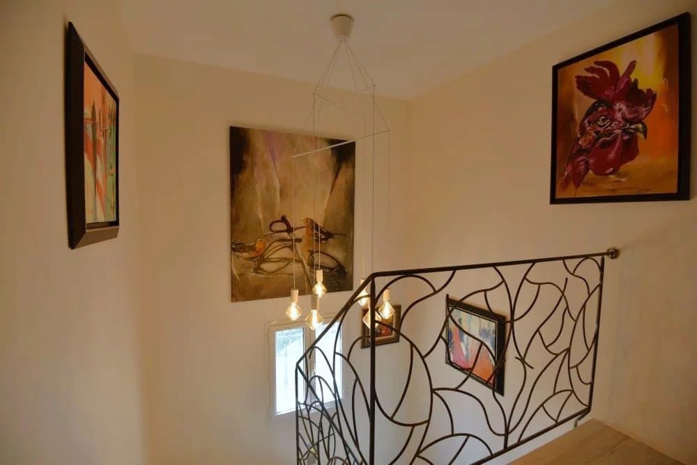 Escalier intérieur d'une villa avec œuvres d'art aux murs et lumière suspendue.