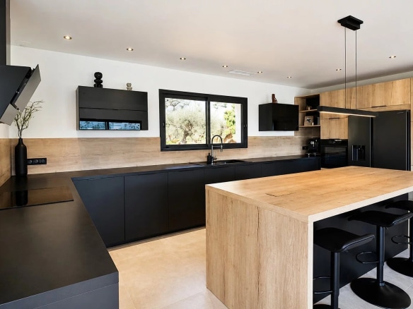 Cuisine moderne et épurée d'une villa contemporaine à Fayence, avec plans de travail en bois et mobilier noir.