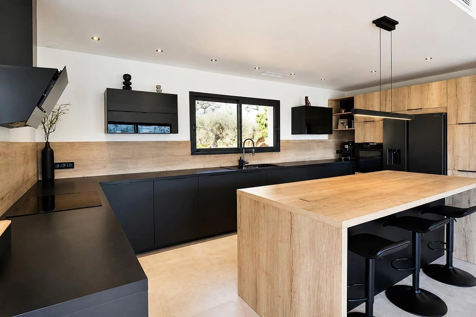 Cuisine moderne et épurée d'une villa contemporaine à Fayence, avec plans de travail en bois et mobilier noir.