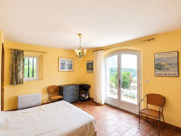 Chambre lumineuse avec vue sur la vallée à Fayence, murs jaunes et mobilier simple.