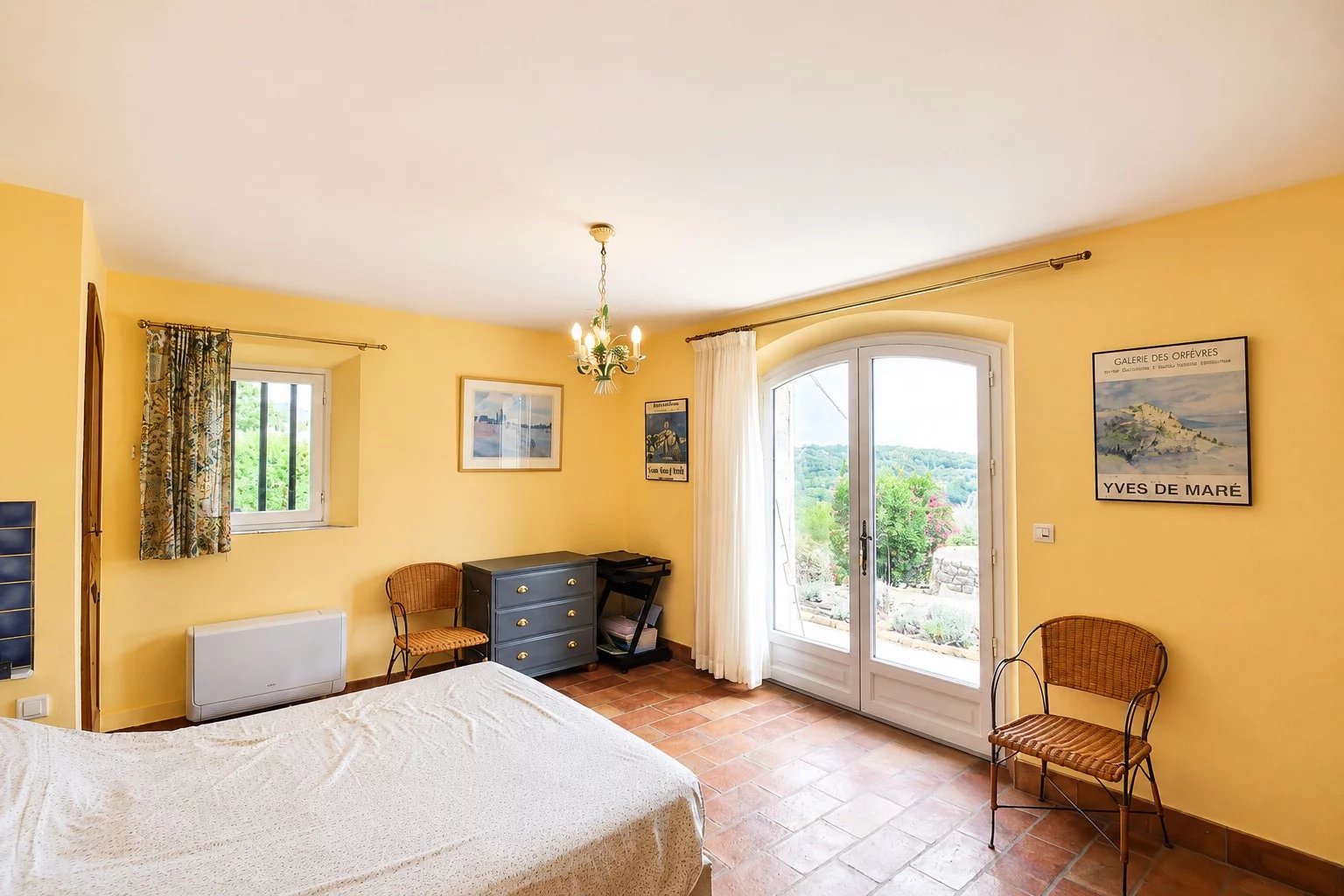 Chambre lumineuse avec vue sur la vallée à Fayence, murs jaunes et mobilier simple.