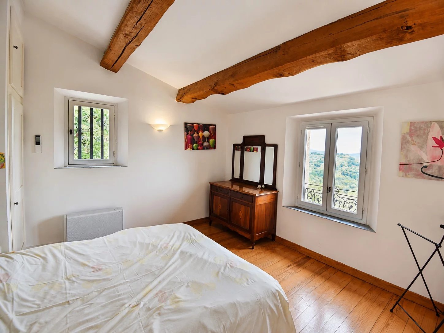 Chambre d'une maison en pierre à Fayence avec vue sur la vallée, fenêtres et poutres apparentes.