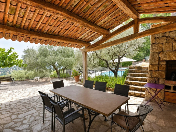 Terrasse couverte avec table et chaises, piscine et oliveraie en arrière-plan à Fayence.
