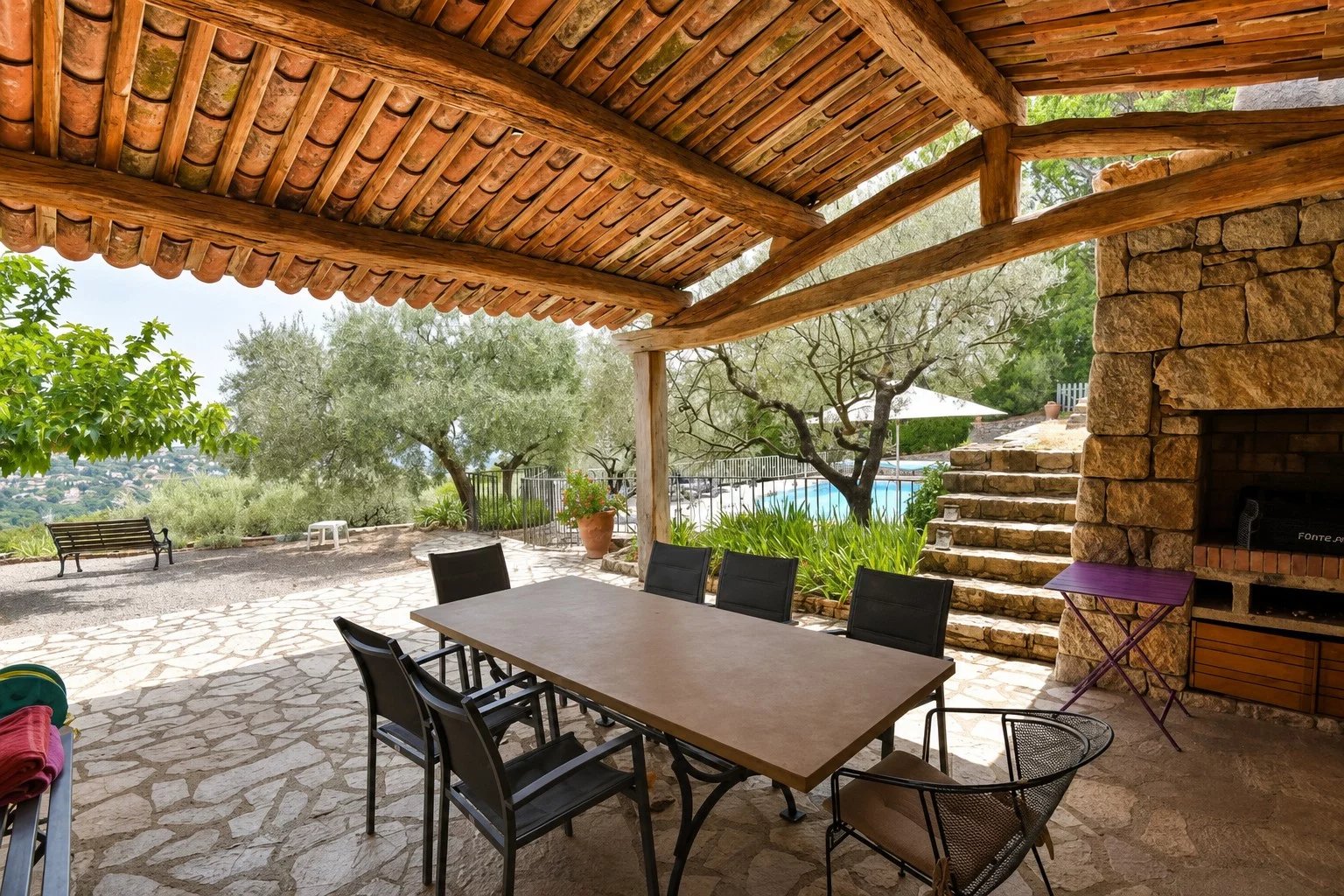 Terrasse couverte avec table et chaises, piscine et oliveraie en arrière-plan à Fayence.