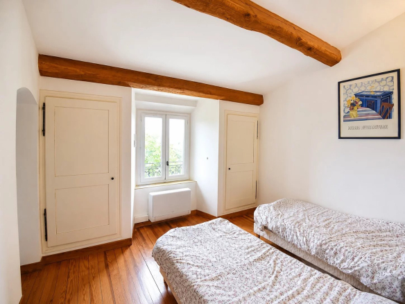 Chambre avec deux lits simples et murs blancs, poutres apparentes en bois.