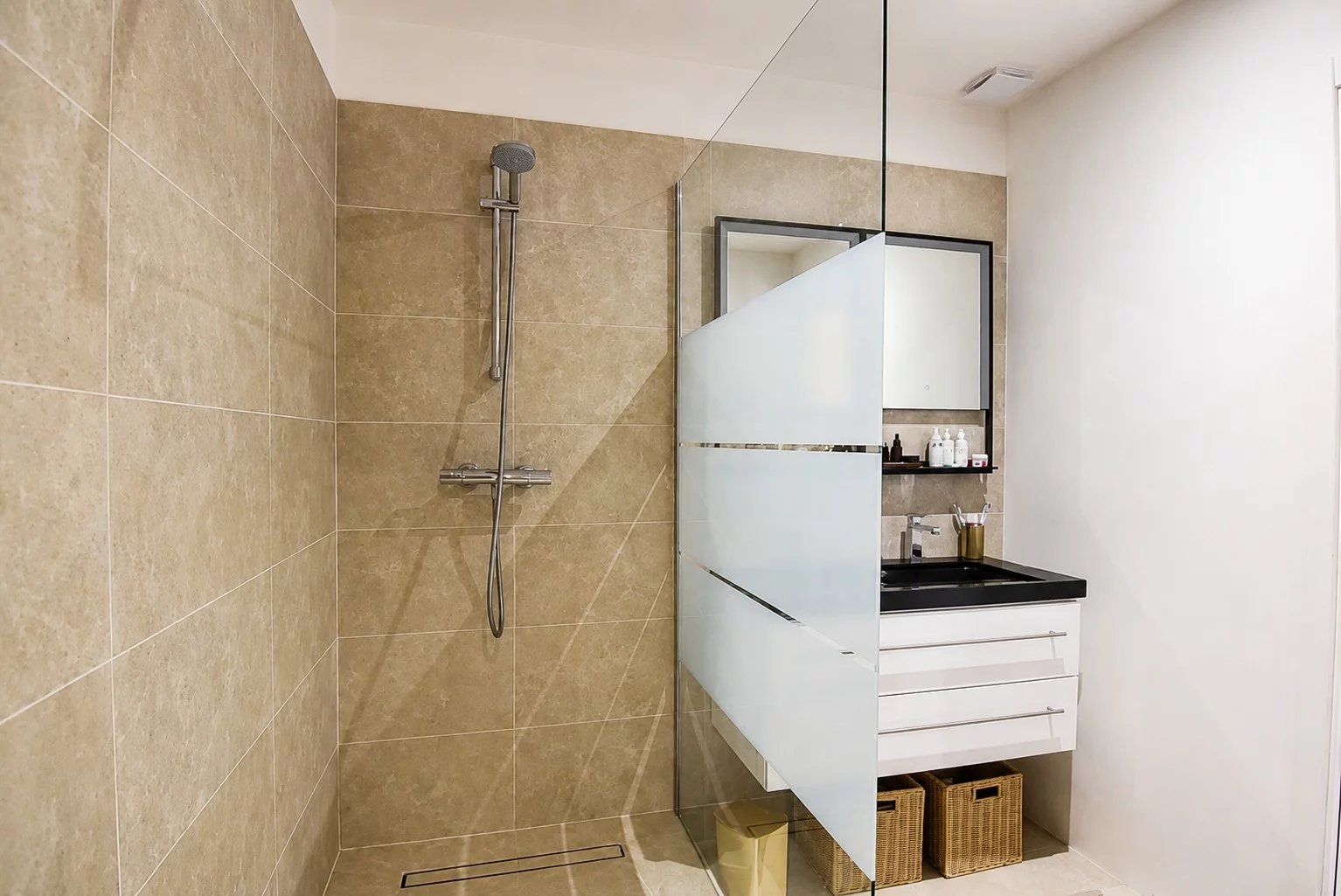 Salle de bain moderne avec douche en verre et meuble sous vasque.