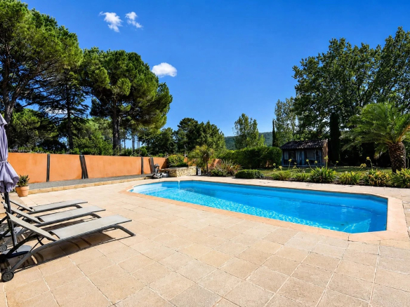 Piscine avec chaises longues dans un jardin verdoyant à Bagnols-en-Forêt.
