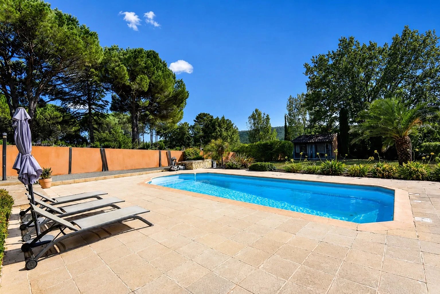 Piscine avec chaises longues dans un jardin verdoyant à Bagnols-en-Forêt.