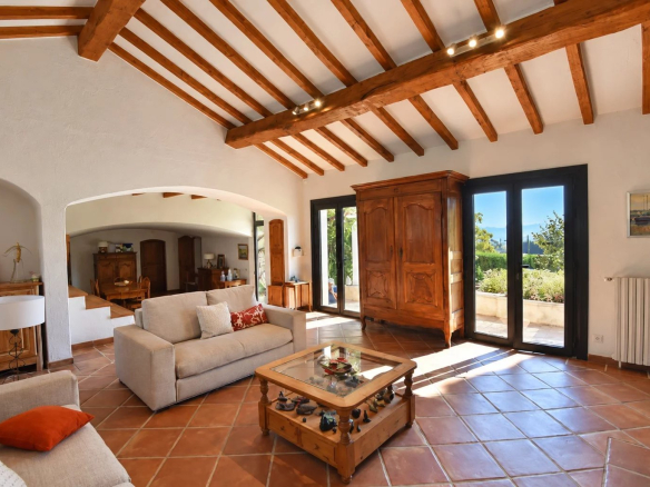 Interior of a Provençal property with a bright living room, exposed beams and a view of the garden.