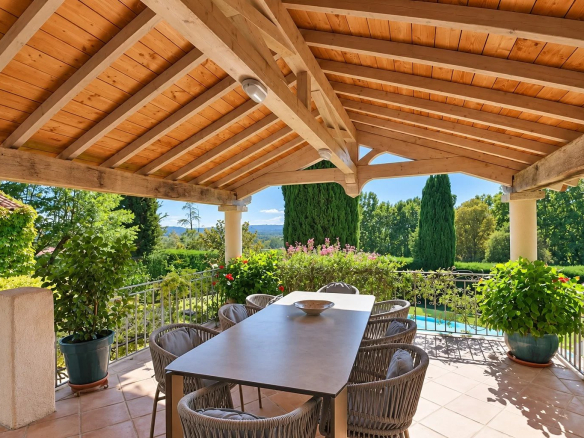 Covered terrace with table and chairs, overlooking the pool and greenery in Callian