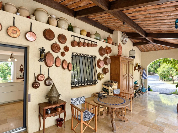 Terrasse couverte d'une villa avec décoration en cuivre et mobilier en bois à Tourrettes.