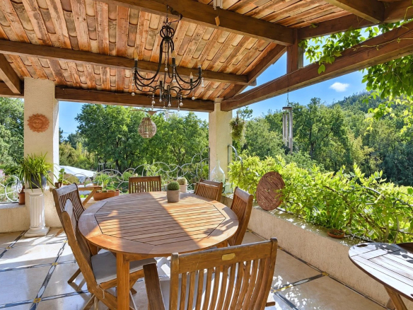 Terrasse en bois avec table et chaises, entourée de verdure, à Tourrettes.