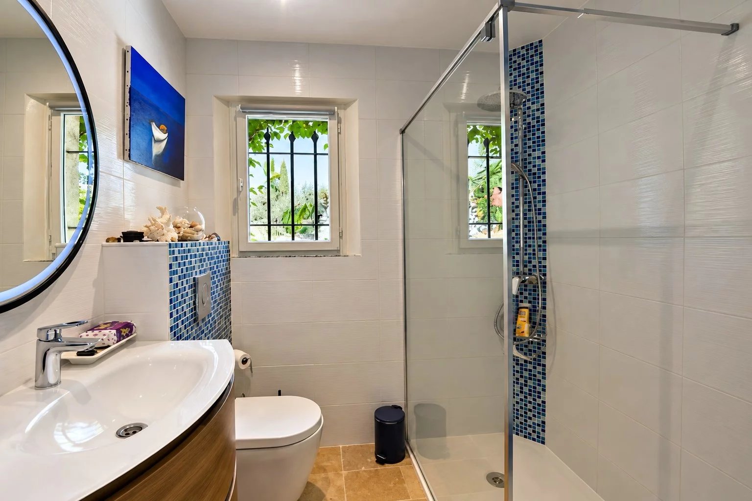 Salle de bain moderne avec douche, lavabo et toilettes, décorée de carrelage blanc et bleu.