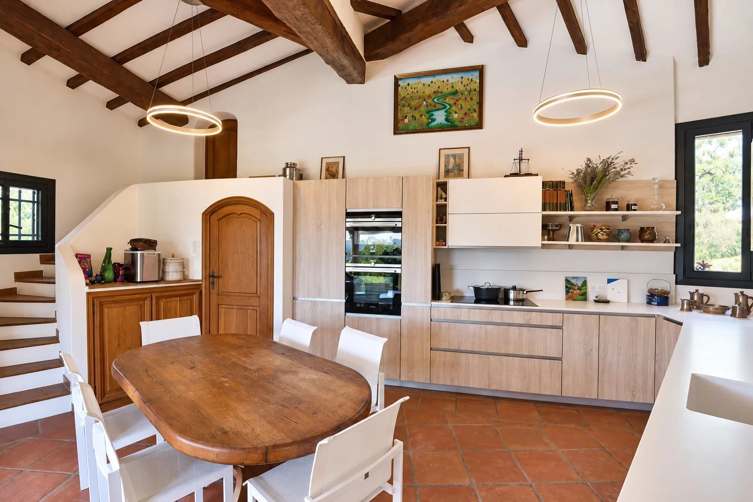 Spacious and bright kitchen Modern kitchen with wooden table and white chairs, exposed beams and windows to the outside.