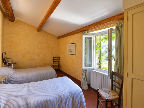 Room with two single beds, windows opening onto a green landscape, yellow walls and exposed beams.
