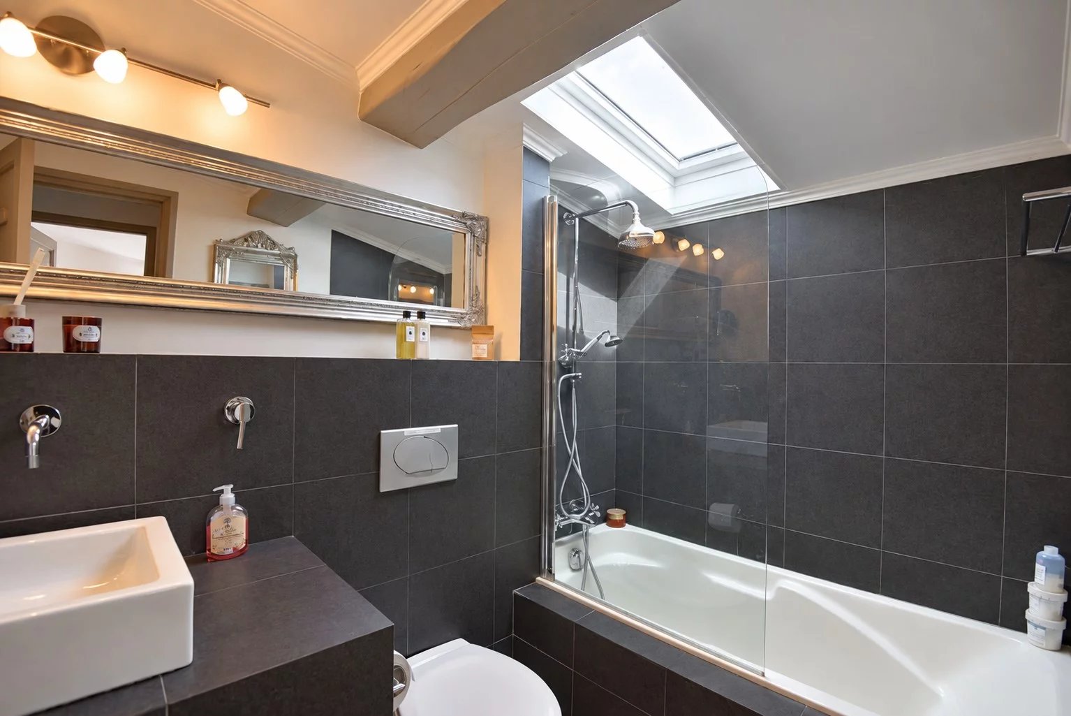 Salle de bain moderne avec baignoire et douche, murs carrelés en noir et blanc.