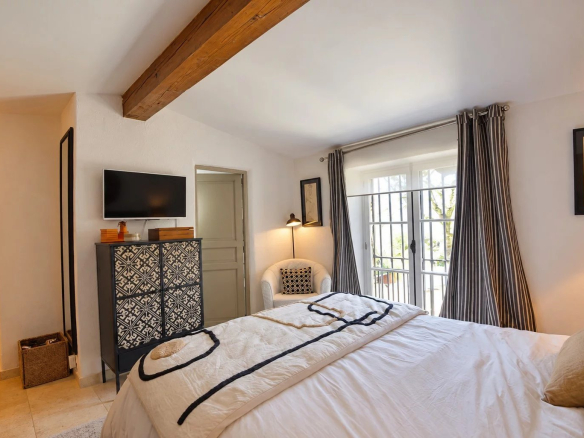 Chambre d'une maison en pierre à Tourrettes, avec lit, meuble et fenêtre donnant sur l'extérieur.