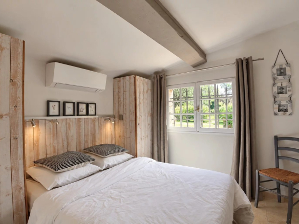 Chambre d'une maison en pierre à Tourrettes, avec lit double et fenêtres donnant sur le jardin.