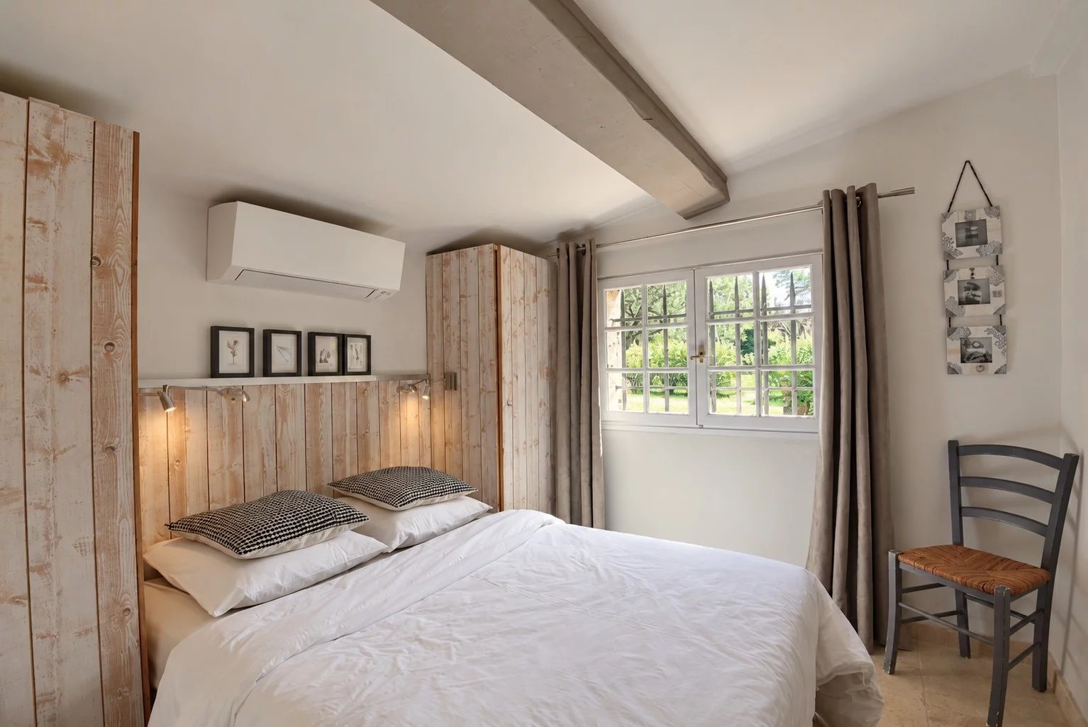 Chambre d'une maison en pierre à Tourrettes, avec lit double et fenêtres donnant sur le jardin.