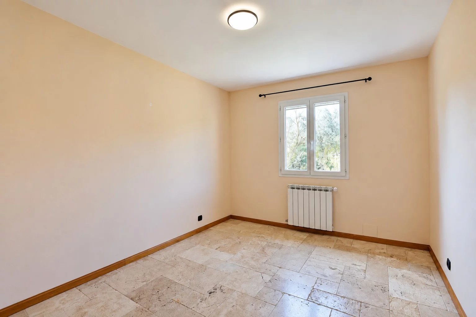 Chambre vide dans une villa provençale Chambre vide avec murs clairs et fenêtre, sol en pierre, radiateur visible.