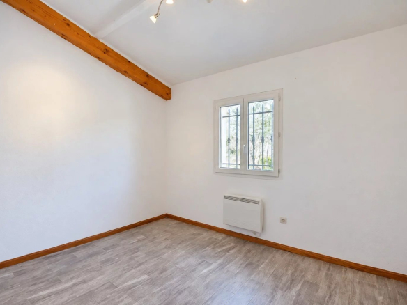 Intérieur d'une pièce vide avec des murs blancs et un sol en parquet, lumière naturelle par la fenêtre.