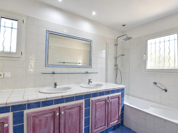 Salle de bain avec deux lavabos, douche et baignoire, carrelage en faïence blanche et bleue.