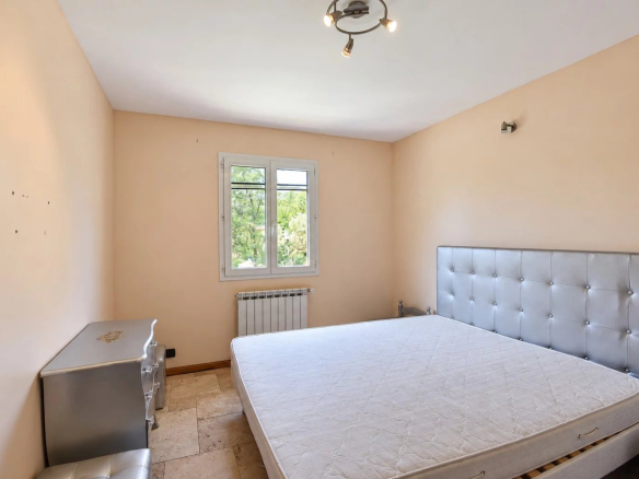 Chambre vide avec lit et fenêtre, murs beige, dans une villa provençale à Fayence.