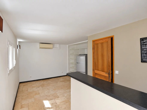 Intérieur d'une villa provençale avec un bar et un réfrigérateur, murs clairs et espace ouvert.