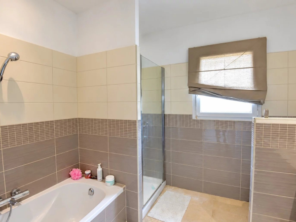 Salle de bain moderne avec baignoire et douche, carrelage clair et fenêtre.
