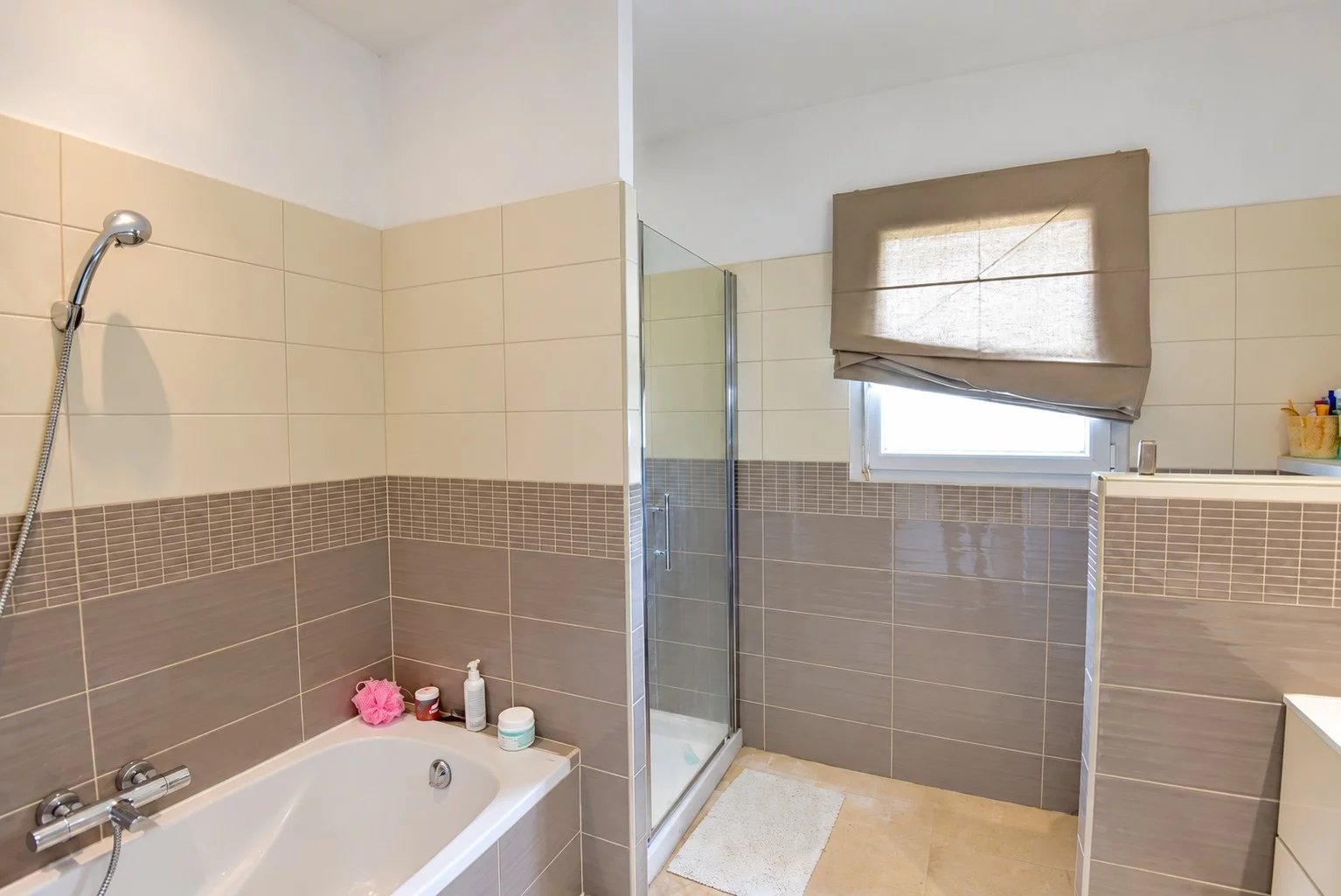 Salle de bain de la villa à Saint-Paul-en-Forêt Salle de bain moderne avec baignoire et douche, carrelage clair et fenêtre.